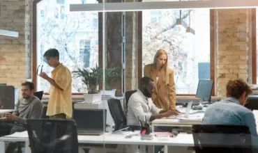 People working in a modern open-plan office with brick walls and large windows.