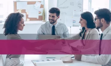 Professionals shaking hands in an office setting with charts on the wall.