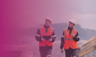 Two people in safety vests and helmets walking at a construction site.